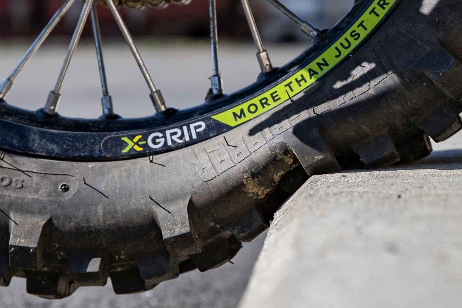 Detail dezénu enduro pneumatiky X-GRIP opřené o betonový blok